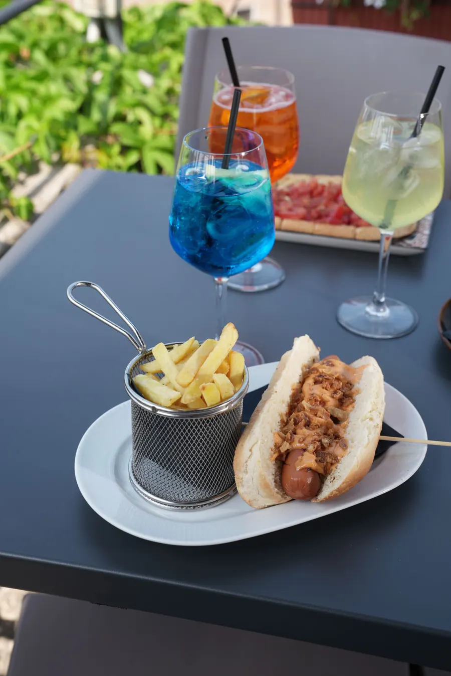 Hot dog con patatine fritte e cocktail colorati sulla terrazza del Kiosko